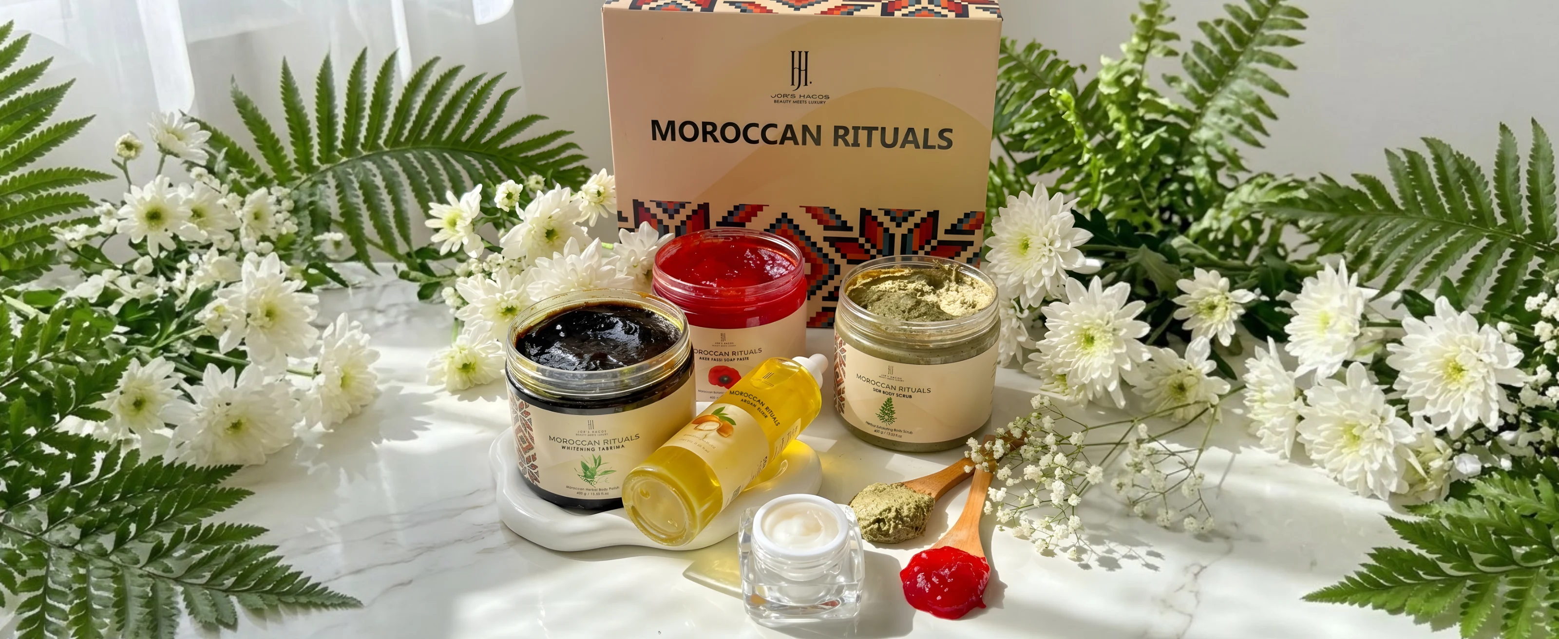 The Moroccan Rituals set: coconut bowls of soap paste and scrub and a bottle of argan oil in front of a box with Moroccan patterns