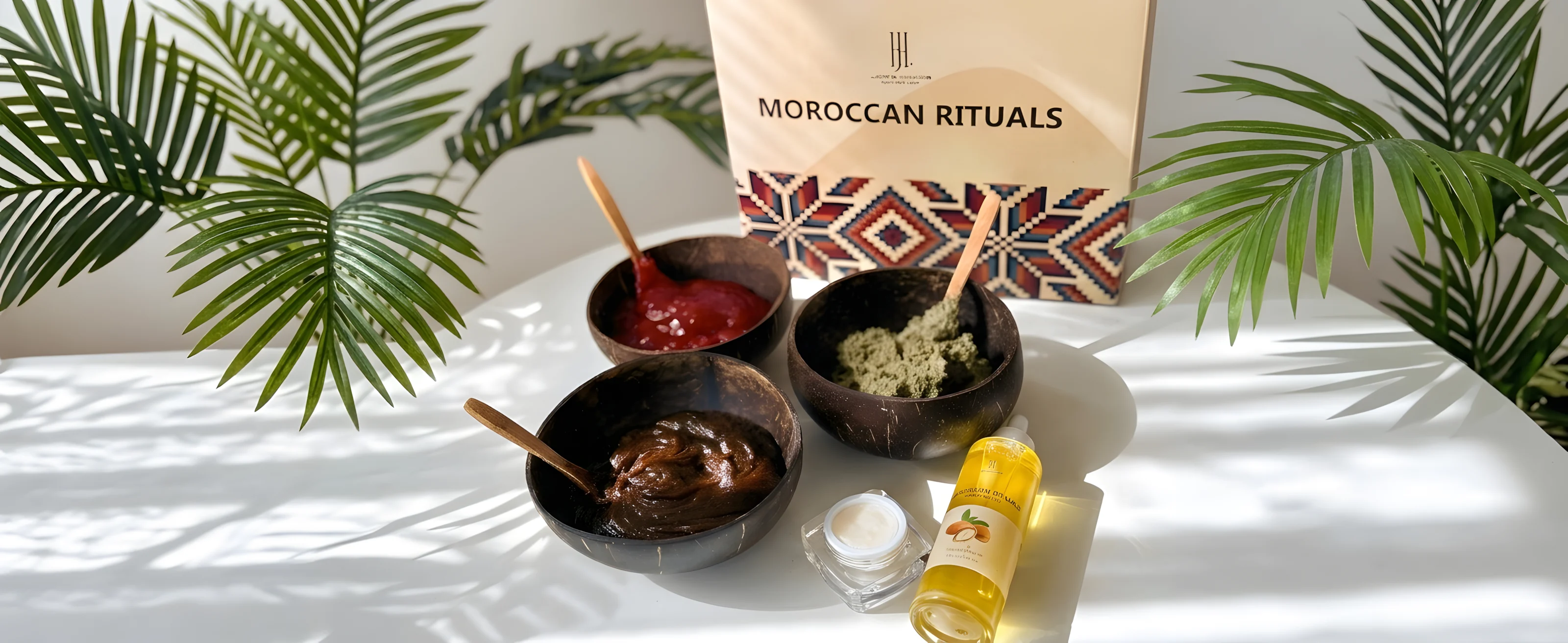 The Moroccan Rituals set: coconut bowls of soap paste and scrub and a bottle of argan oil in front of a box with Moroccan patterns